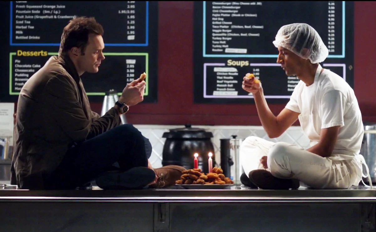 Jeff y Abed comiendo alitas de pollo encima de una mesada. 